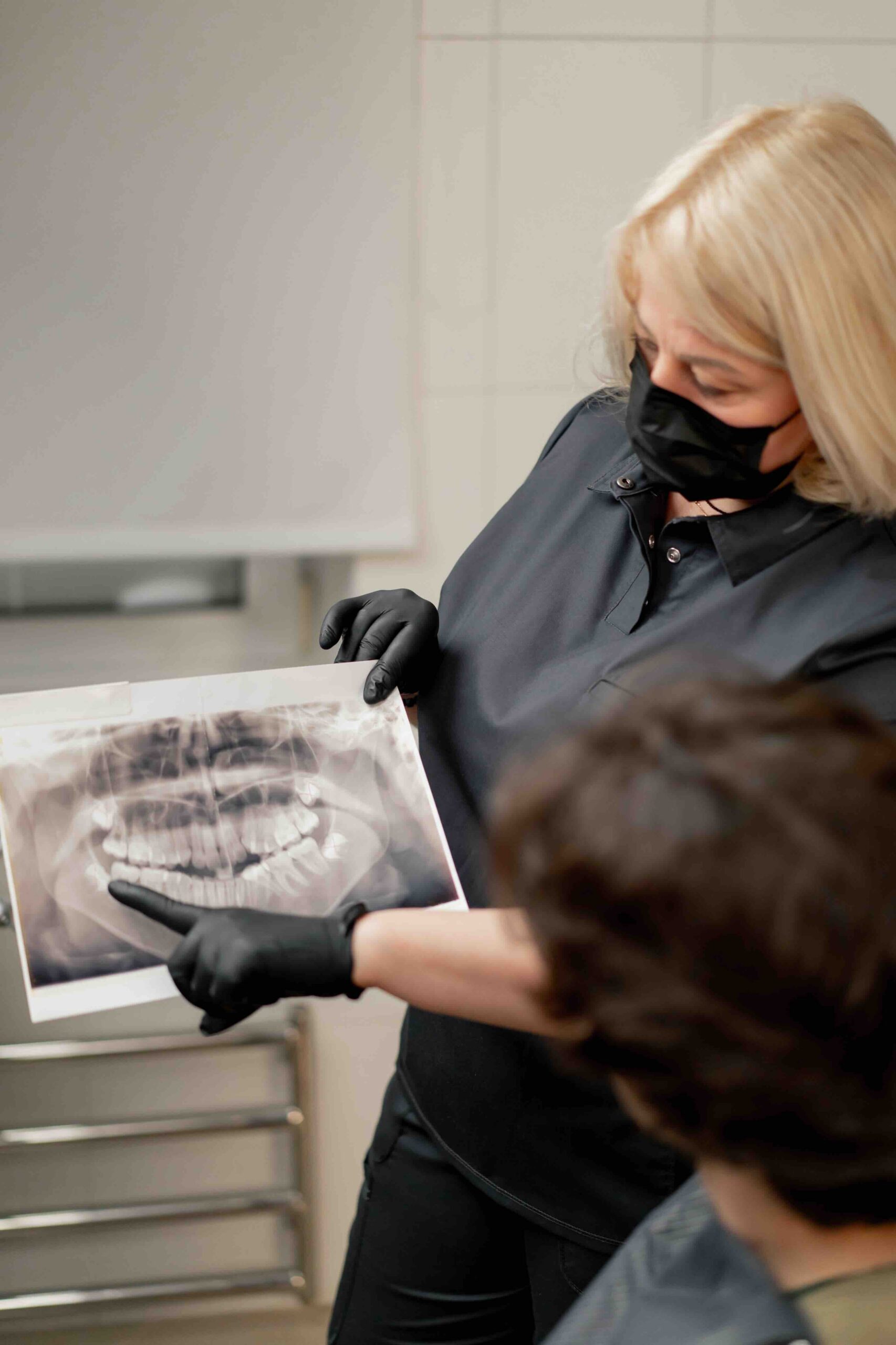 dental office blonde dentist in a black uniform consulting patient showing a photo of the teeth